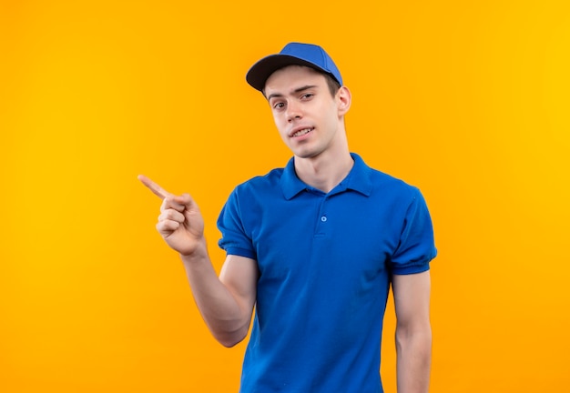 Young courier wearing blue uniform and blue cap point happily on the right with forefinger