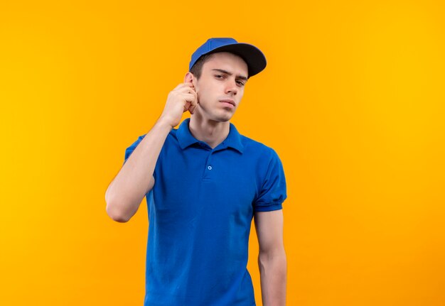 Young courier wearing blue uniform and blue cap scratches ear