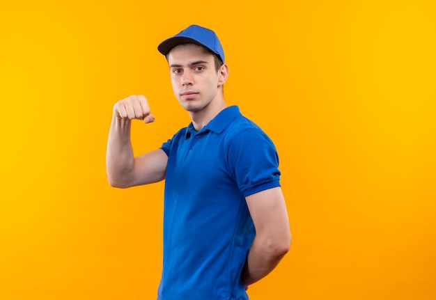 Young courier wearing blue uniform and blue cap shows power with fist
