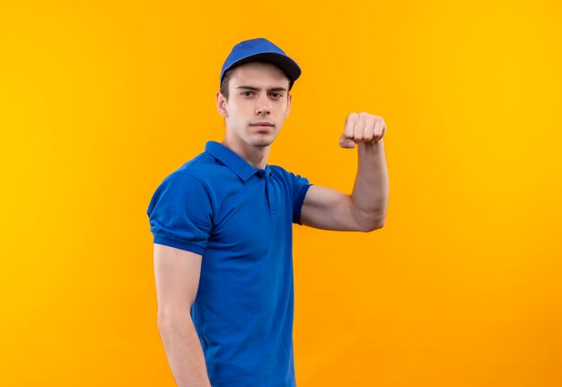 Young courier wearing blue uniform and blue cap shows power with fist