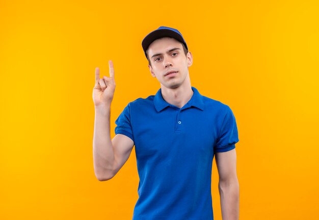 Молодой курьер в синей форме и синей кепке показывает рок пальцами