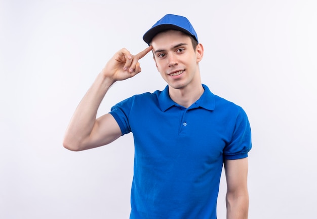 Foto gratuita il giovane corriere che indossa l'uniforme blu e il berretto blu sorride e pensa