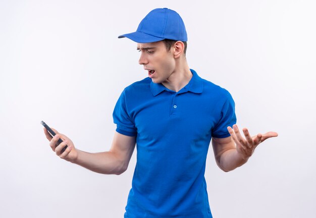 파란색 유니폼과 파란색 모자를 쓰고 젊은 택배가 전화를 쳐다 본다.