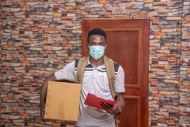 Young courier wearing a medical mask and holding a package and documents