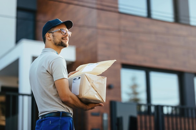 Young courier with packages looking for the right address while making home delivery