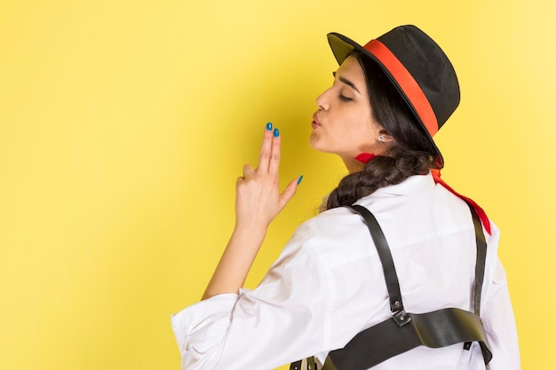 Free photo young cowgirl standing on yellow background and holding her hand as a gun high quality photo