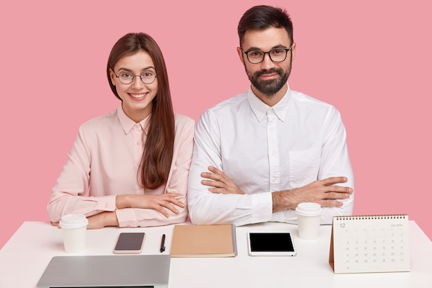 Free photo young coworkers sitting at desk with gadgets and calendar