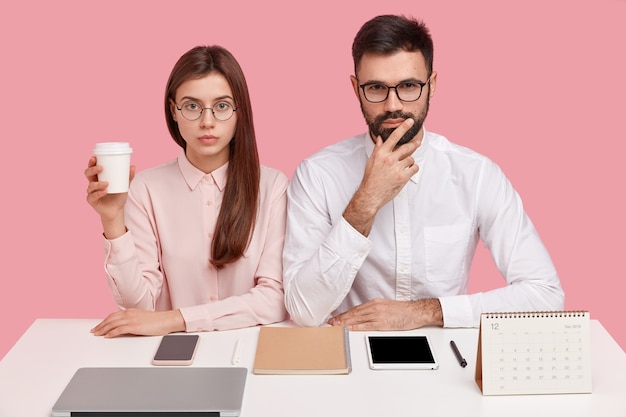 Young coworkers sitting at desk with gadgets and calendar