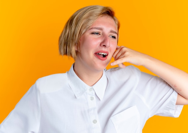 young crying blonde russian girl gestures call sign isolated on orange background with copy space