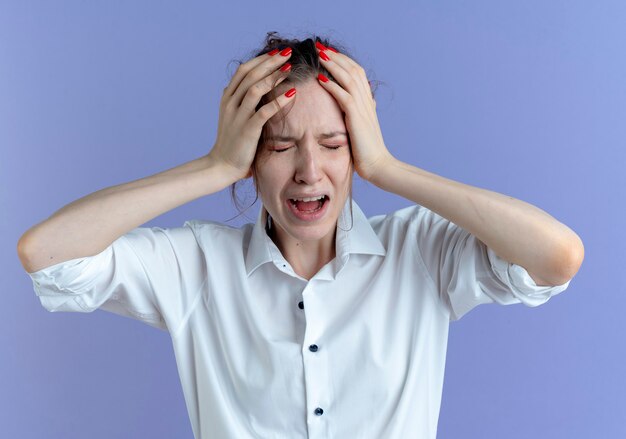 Young crying blonde russian girl holds head on purple  with copy space