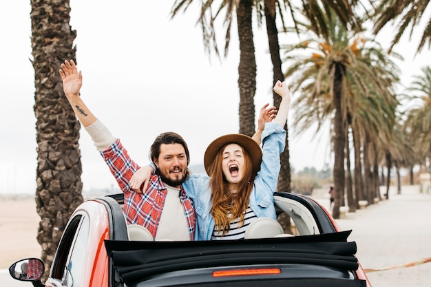 Young crying woman and happy man with upped hands hugging and leaning out from car