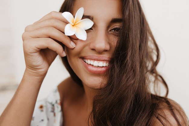 Young curly brunette woman covers her eyes with white flower