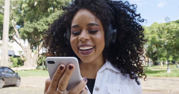 Молодая чернокожая женщина вьющихся волос, идущая с помощью мобильного телефона текстовые сообщения на улице. большой город.