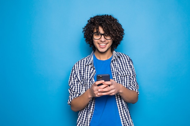 Young curly handsome man typing on the phone over isolated on blue wall