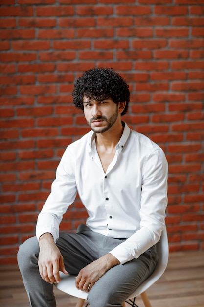 Young curly handsome in white shirt sitting on white chair. High quality photo