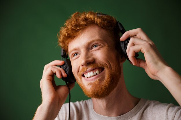 Young curly readhead bearded man is enjoying listening to music