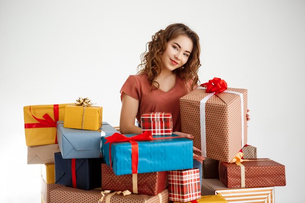 Young curly woman among gift boxes on white