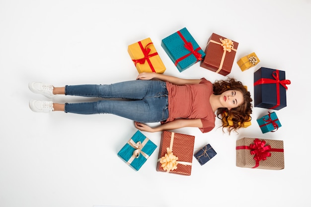 Young curly woman lying on floor among gift boxes