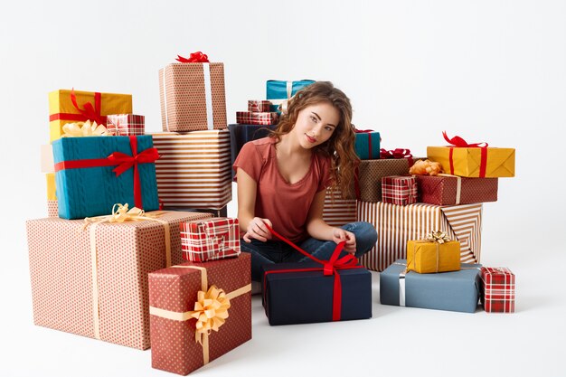 Young curly woman sitting on floor among gift boxes opening one of them