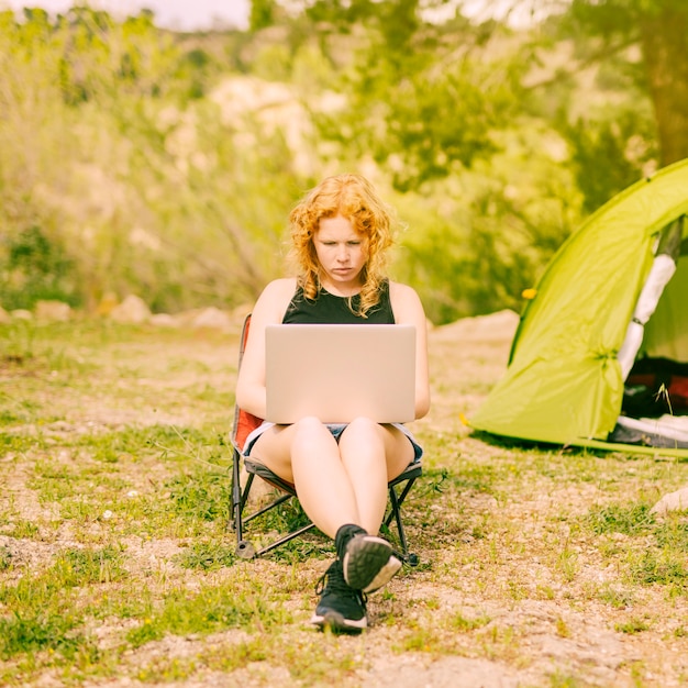 Young curly woman surfing on laptop on nature