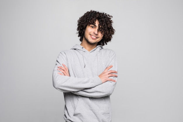 Young curly young man with crossed hands isolated on white wall