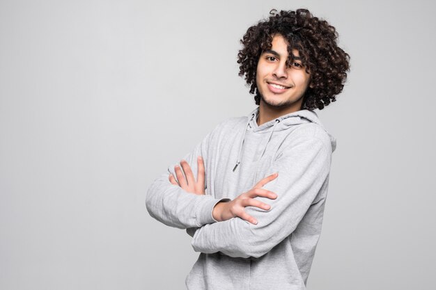 Young curly young man with crossed hands isolated on white wall