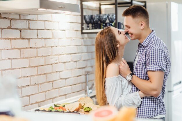Young, cute couple having nice time together at the kitchen, hugging together and kissing..