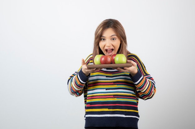 Free photo a young cute girl model holding a wooden plate with colorful fresh apples .