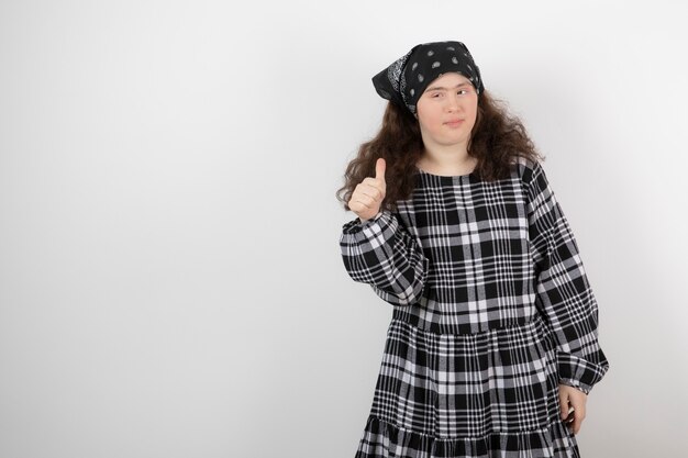 young cute girl with down syndrome standing and showing a thumb up .