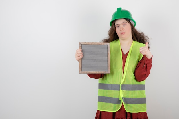 young cute girl with down syndrome standing in vest and holding a frame .