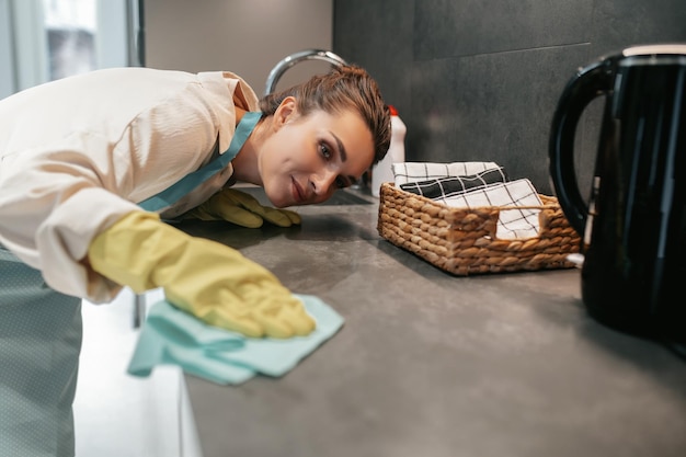 Giovane donna dai capelli scuri che pulisce le superfici in cucina