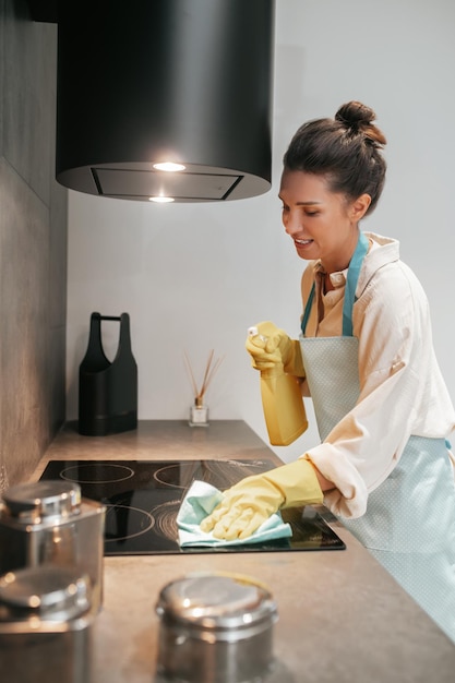 Молодая темноволосая женщина дезинфицирует поверхности на кухне