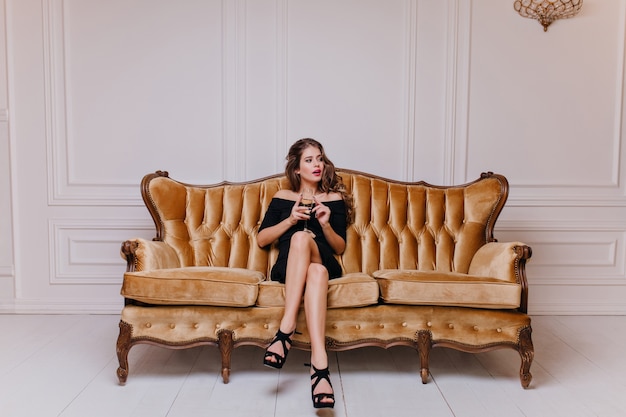 Free photo young dark-haired woman, sitting on huge golden sofa, surrounded by soft pillows and looking to  left