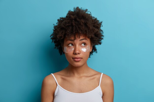 young dark skinned woman with Afro hair applies hydrogel silver patches under eyes, reduces puffiness, removes dark circles. Skin care concept