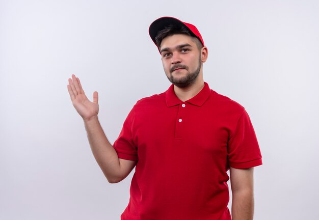 Young delivery boy in red uniform and cap presenting copy space with arm of his hand looking confident 