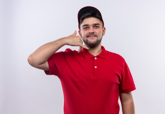 Young delivery boy in red uniform and smiling confident making call me gesture 