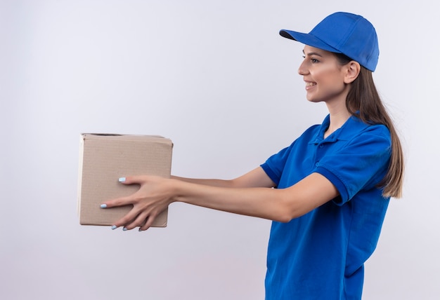 Молодая доставщица в синей униформе и кепке дарит упаковку клиенту, дружелюбно улыбаясь