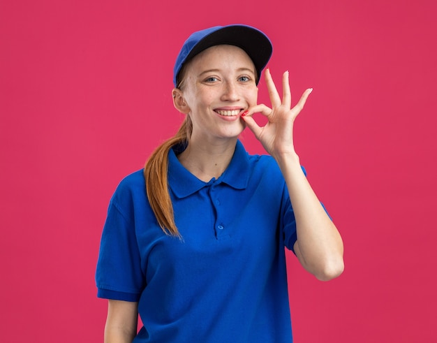 Young delivery girl in blue uniform and cap   happy and cheerful making silence gesture like closing mouth with a zipper