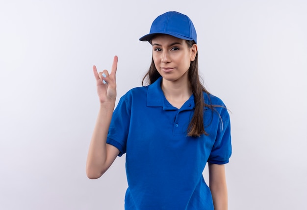 Молодая доставщица в синей форме и кепке выглядит уверенно, показывая рок-символ пальцами
