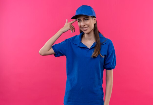 Молодая доставщица в синей униформе и кепке выглядит сбитой с толку, указывая висок на ошибку