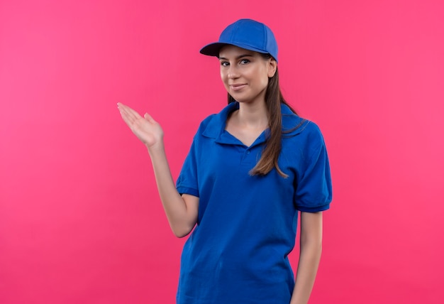 Young delivery girl in blue uniform and cap presenting with arm of hand copy space 