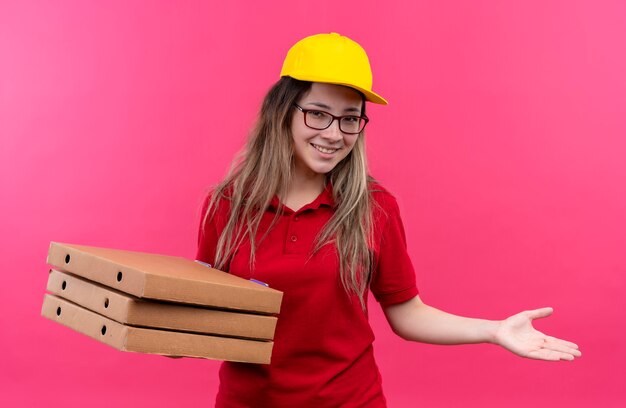 빨간색 폴로 셔츠와 넓게 웃고있는 피자 상자를 들고 노란색 모자에 젊은 배달 소녀