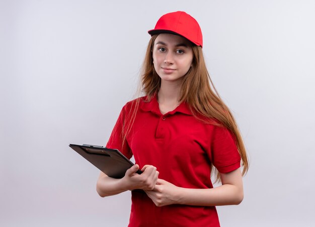 Young delivery girl in red uniform holding clipboard and on isolated white wall