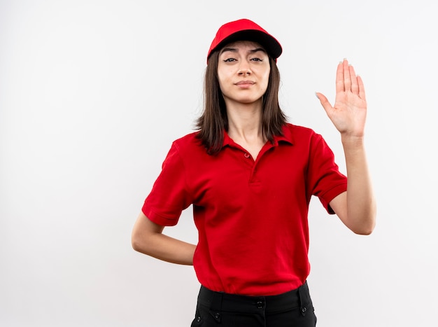 Free photo young delivery girl wearing red uniform and cap looking at camera with serious face making stop sign with open hand standing over white background