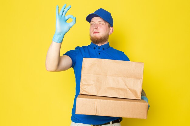 young delivery man in blue polo blue cap white jeans backpack holding boxes on yellow