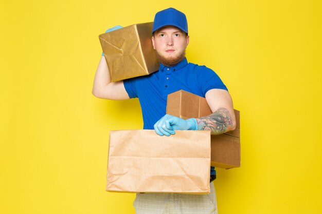 молодой доставщик в синей рубашке поло синяя кепка белый джинсовый рюкзак держит коробки на желтом