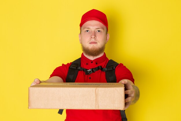 young delivery man in red polo red cap white jeans holding a box on yellow