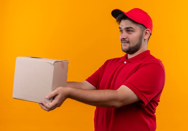 Young delivery man in red uniform and cap giving box package to a customer smiling friendly