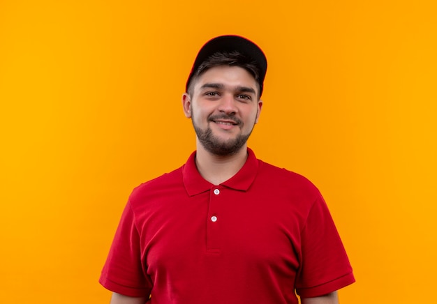 Young delivery man in red uniform and cap looking at camera with smile on face