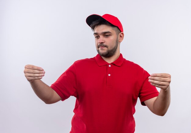 Young delivery man in red uniform and cap looking confident gesturing with hands, body language concept 